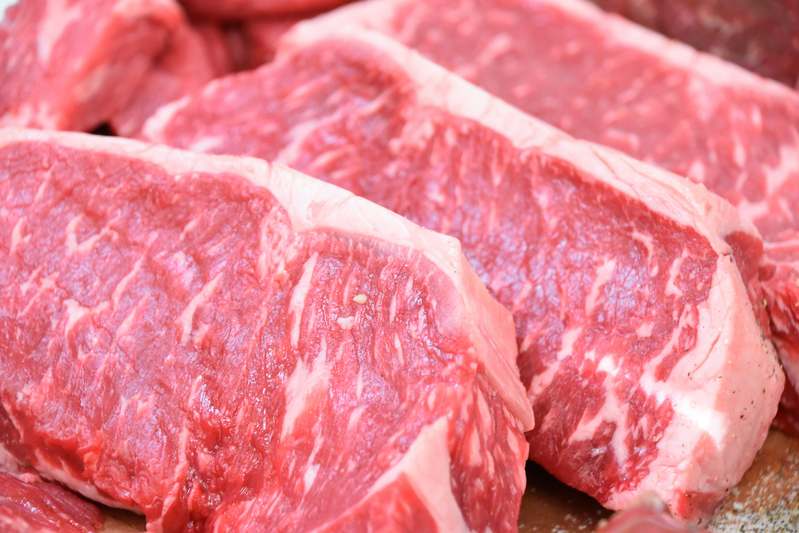 Close-up of hands operating a stainless steel manual meat grinder on a wooden countertop with freshly ground beef beside it